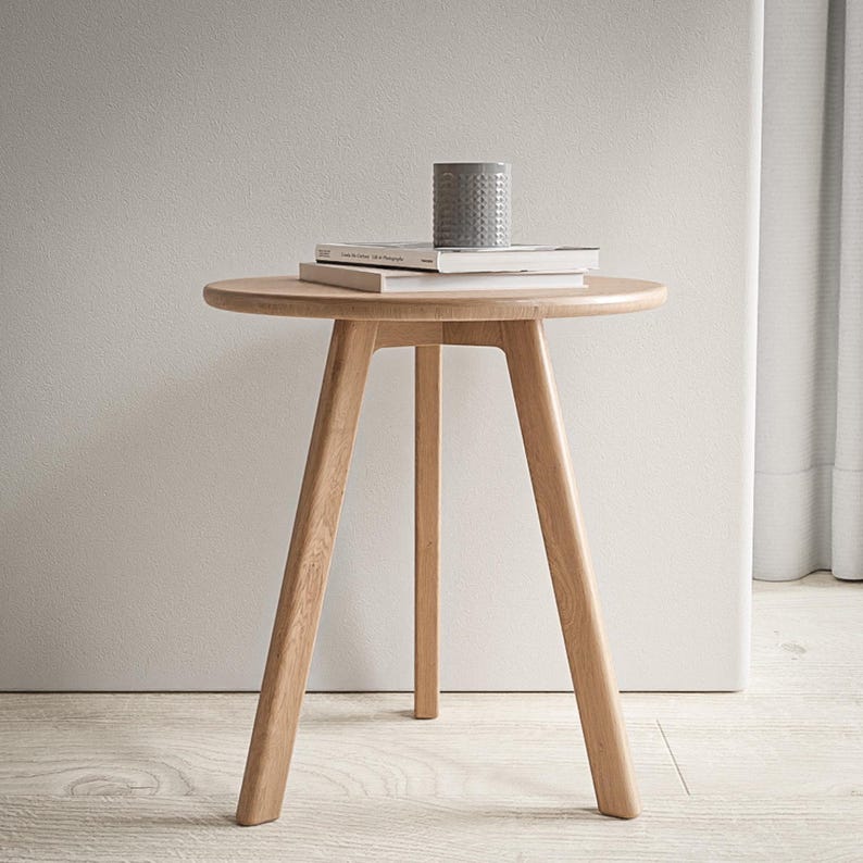 Puede incluir: Una mesa auxiliar redonda de madera clara con tres patas. La mesa tiene un acabado de madera natural y est&aacute; hecha de madera maciza. La mesa tiene un di&aacute;metro de 61 cm y una altura de 51 cm.