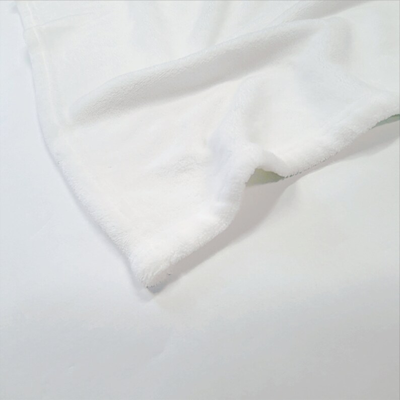 May include: Close-up of a white fleece blanket with a soft, fluffy texture. The blanket is folded and the edge is visible.