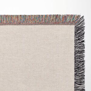 May include: A beige woven throw blanket with a multicoloured fringe border and black fringe on the sides.