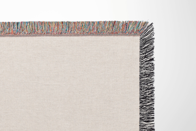 May include: A beige woven throw blanket with a multicoloured fringe border and black fringe on the sides.