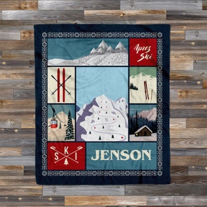 May include: A blue and red fleece blanket with a winter mountain scene and the text "Après Ski" and "Jenson". The blanket is divided into squares with images of ski slopes, a ski lift, and skis.