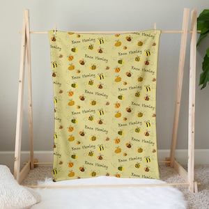 May include: A yellow baby blanket with a repeating pattern of bees and the name "Knox Henley" printed on it.