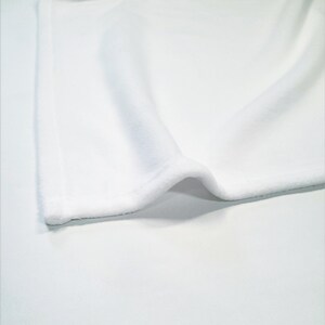 May include: White fabric with a soft, fuzzy texture. The fabric is folded over on itself, showing the edge of the material.