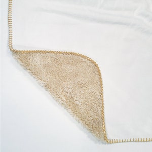 May include: A white blanket with a tan fleece lining. The blanket has a gold stitched border.