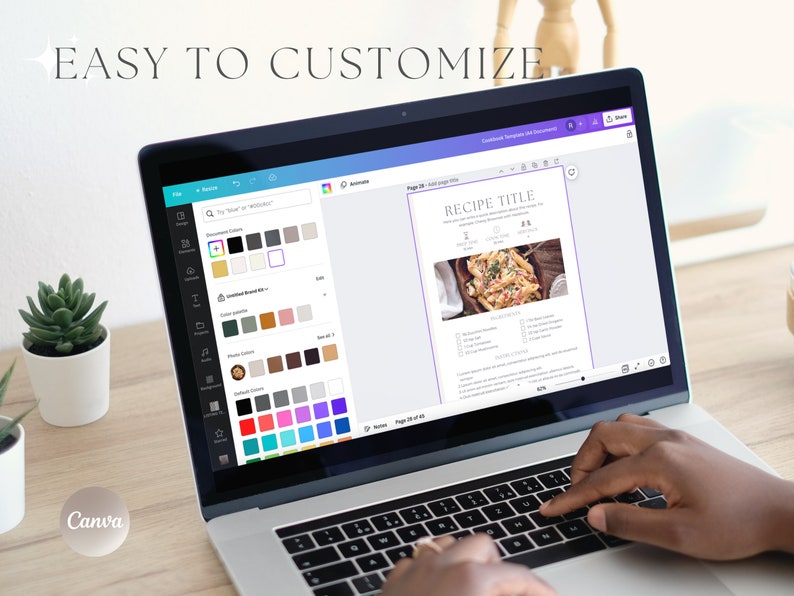 May include: A laptop computer with a white background and the Canva logo on the bottom left corner. The screen shows a recipe template with a photo of pasta with a white background and the text "RECIPE TITLE" in a purple box. The laptop keyboard is visible with a person's hand typing on it.