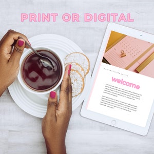 May include: A white tablet displaying a welcome message with pink text and a pink calendar on the screen. A person is holding a cup of tea and a spoon in their hands. The tablet is on a white wooden surface.