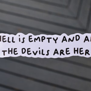Puede incluir: Una pegatina blanca con la cita "HELL is EMPTY AND ALL OF THE DEVILS ARE HERE." en texto negro. La pegatina la sostiene una persona con esmalte de uñas negro.