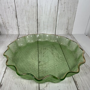 May include: A green glass pie plate with a gold rim and a scalloped edge. The plate has a textured surface.