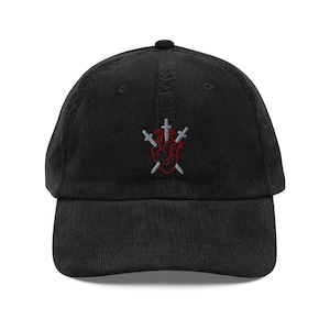 May include: A black corduroy baseball cap featuring an embroidered design on the front center. The embroidery depicts a red anatomical heart pierced by three silver-colored swords arranged in a fan-like pattern across the heart shape.