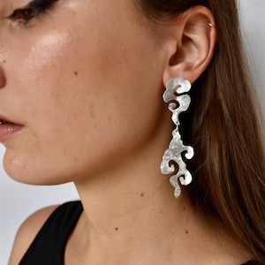 May include: Silver dangle earrings with a textured, abstract cloud design.