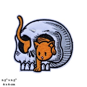 May include: An embroidered iron-on patch featuring a white skull with a small orange cat peeking out from inside. The patch is 2.5 inches by 2.5 inches, or 6 centimetres by 6 centimetres.