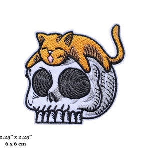 Peut inclure: Patch brodée thermocollante représentant un crâne blanc sur lequel dort un chat orange. La taille du patch est de 6 cm sur 6 cm.