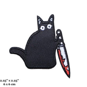 Pode incluir: Gato preto com olhos brancos segurando uma faca vermelha e branca. O gato está sentado em um fundo branco. O remendo mede 6 cm por 6 cm.