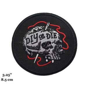 Puede incluir: Parche bordado en blanco y negro con una calavera y el texto "DIY or DIE" en un círculo. La calavera está cosida con hilo rojo.