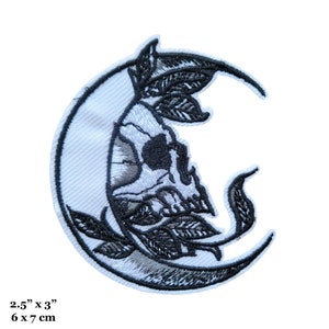 May include: Black and white embroidered patch of a skull inside a crescent moon with leaves. The patch is 2.5 inches by 3 inches and 6 cm by 7 cm.