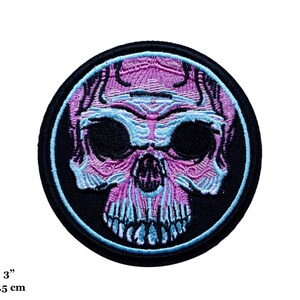 May include: Embroidered patch featuring a stylized skull design. The skull is rendered in shades of purple and light blue, set against a black background. The patch is round, approximately 3 inches (7.5 cm) in diameter, and suitable for application on clothing or accessories.