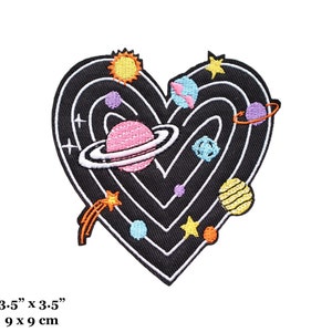 May include: Embroidered iron-on patch featuring a black heart with a swirling galaxy design. The heart is filled with colorful planets, stars, and a comet. The patch measures 3.5 inches by 3.5 inches.