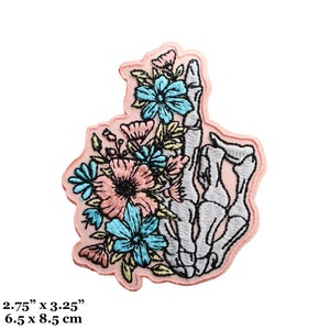 Pode incluir: Um remendo bordado para passar a ferro com uma mão de esqueleto segurando um buquê de flores rosa e azuis. O remendo mede 2,75 polegadas por 3,25 polegadas e 6,5 cm por 8,5 cm.