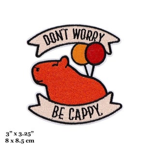 May include: Embroidered iron-on patch featuring a cartoon capybara holding two balloons with the text "Don't Worry Be Cappy" in a white banner. The patch is 3 inches by 3.25 inches.