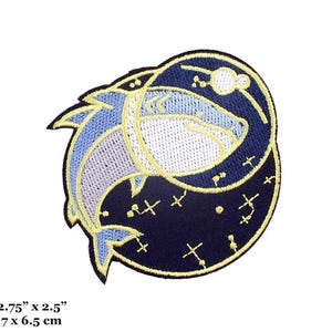 May include: A blue and white embroidered patch of two fish swimming in a circle with a black background and yellow stars. The patch is 2.75 inches by 2.5 inches.
