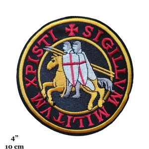 Peut inclure: Un écusson rond brodé avec un fond noir et une bordure dorée. Au centre de l'écusson, une croix blanche et deux chevaliers à cheval. Le texte "XPISTI SIGILLVM MILITVM" est écrit en rouge autour du bord de l'écusson.