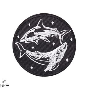 May include: Black and white embroidered patch of a shark and a whale on a black background. The patch is 7.5 cm in diameter.