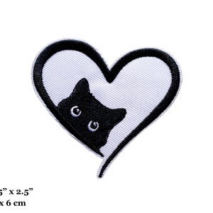 May include: Black and white embroidered iron-on patch of a cat peeking out of a heart. The patch measures 2.75 inches by 2.5 inches or 7 cm by 6 cm.