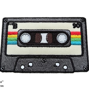 Könnte beinhalten: Ein schwarzer und weißer Kassettenband-Patch mit einem Regenbogenstreifen und dem Text "90" auf der rechten Seite. Der Patch ist 3,25 Zoll mal 2,2 Zoll groß, das sind 8,5 cm mal 5,5 cm.