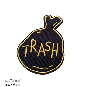 May include: A black and gold embroidered iron-on patch with the word "TRASH" in a gold outline on a black trash bag shape. The patch is 1.75 inches by 2.4 inches.