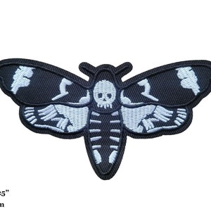 May include: Black and white embroidered iron-on patch of a moth with a skull design. The moth is 4.5 inches by 2.25 inches, or 11 cm by 6 cm.