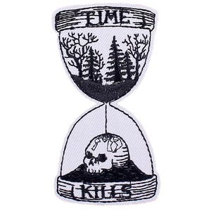 May include: Black and white embroidered iron-on patch of an hourglass with a skull at the bottom. The hourglass is filled with a forest scene and the words "Time Kills" are on the top and bottom of the hourglass.
