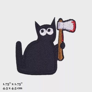 May include: Black cat with large white eyes holding a brown axe with a red handle and a red blood stain on the blade. The cat is 1.75 inches by 1.75 inches.