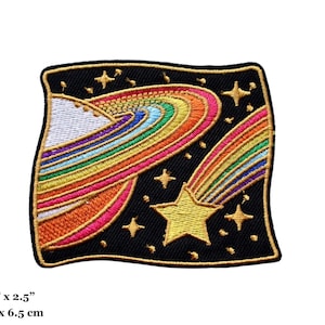 May include: A colorful embroidered patch with a rainbow comet shooting past a planet with a rainbow ring. The patch is set against a black background with gold stars.