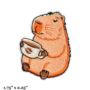 Peut inclure: Patch brodée thermocollante représentant un capybara de dessin animé tenant une tasse de café. Le capybara est orange et brun, et la tasse de café est blanche avec des grains de café bruns à l'intérieur. Le patch mesure 4,5 cm sur 5,5 cm.