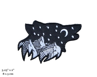 May include: Black and white embroidered patch of a wolf's head with a crescent moon and stars. The wolf's head is filled with a mountain range design. The patch measures 8 cm by 5 cm.