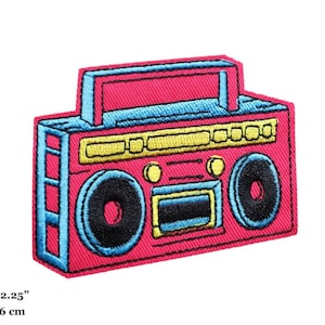 Puede incluir: Parche de estilo retro con una radio rosa con detalles en azul y amarillo. Mide 8 cm x 6 cm. El diseño incluye detalles de altavoces y un asa, ideal para personalizar ropa o accesorios con un toque vintage.
