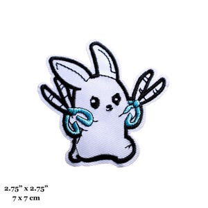 May include: White embroidered iron-on patch of a cartoon bunny holding two blue dragonfly wings. The patch is 2.75 inches by 2.75 inches, or 7 cm by 7 cm.