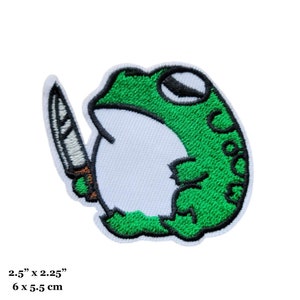 Puede incluir: Parche verde bordado para planchar con una rana sosteniendo un cuchillo. La rana es verde con el vientre blanco y ojos negros. El cuchillo es plateado con mango marrón. El parche mide 6 cm por 5,5 cm.
