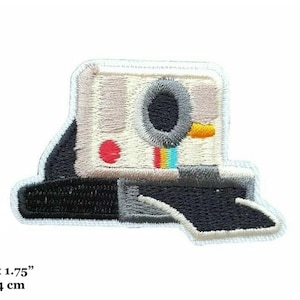 May include: White embroidered iron-on patch of a vintage camera with a rainbow stripe. The patch is 2.5 inches by 1.75 inches, or 6 cm by 4 cm.