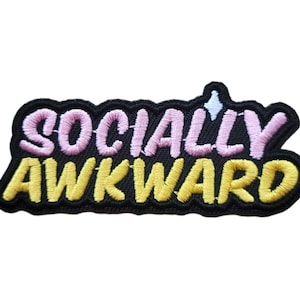 May include: An iron-on patch made of black fabric with the text "SOCIALLY AWKWARD" embroidered in pink and yellow. The patch measures 7.5 cm by 3 cm.