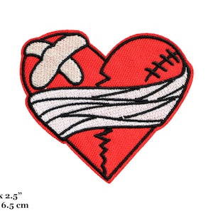 May include: A red heart-shaped patch with a white bandage and stitches. The heart is broken and the bandage is wrapped around it. The patch is 7.5 cm by 6.5 cm.