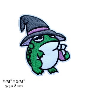May include: An embroidered iron-on patch of a green frog wearing a purple and grey witch hat and holding a purple potion bottle. The patch is 5.5 cm by 8 cm.