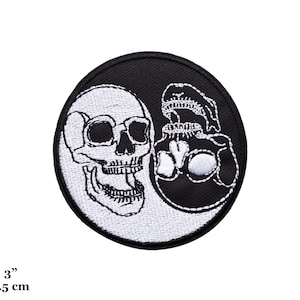May include: Black and white embroidered patch of two skulls in a yin yang design. The patch is 3 inches in diameter.