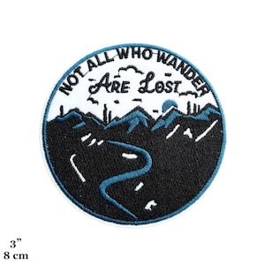 Puede incluir: Un parche bordado blanco y negro con una escena de montaña azul y el texto "Not All Who Wander Are Lost" en negro. El parche tiene un diámetro de 8 cm.