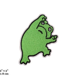 May include: A green embroidered patch featuring a cartoon creature with a black outline and white border. The patch measures 2.25 inches by 3 inches.