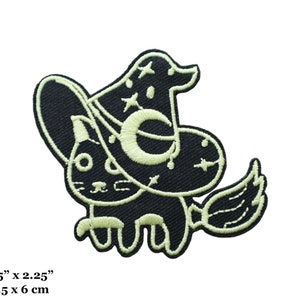 May include: Black and white embroidered iron-on patch of a cat wearing a witch's hat with a crescent moon and stars. The cat is riding a broomstick. The patch is 2.5 inches by 2.25 inches.