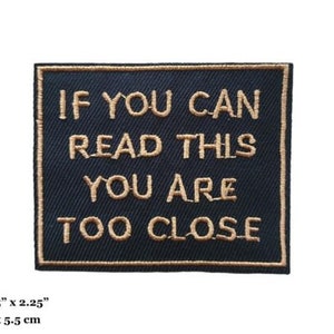 May include: Black embroidered patch with gold text that reads "If you can read this you are too close". The patch measures 7 cm by 5.5 cm.