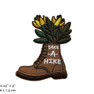 May include: Embroidered iron-on patch featuring a brown hiking boot with yellow flowers sticking out of the top. The boot has the text "TAKE A HIKE" written on it. The patch is 2.25 inches by 3 inches.