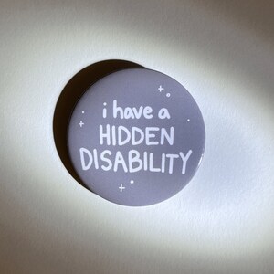 Puede incluir: Un bot&oacute;n gris con texto blanco que dice "i have a HIDDEN DISABILITY".