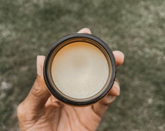 Könnte beinhalten: Ein kleines, rundes Glas mit braunem Deckel und einer weißen, cremigen Substanz darin. Das Glas wird in einer Hand gehalten.